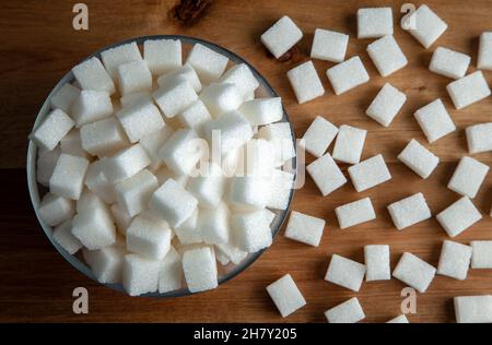 Weiße Zuckerwürfel in Glasschüssel, auf Holzhintergrund Stockfoto