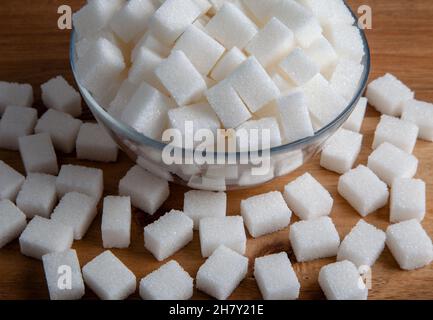 Weiße Zuckerwürfel in Glasschüssel, auf Holzhintergrund Stockfoto