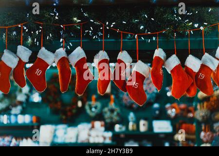 Hängender Adventskalender in Form von hängenden roten Strümpfen. Weihnachtsdekoration. Traditionelle festliche Einrichtung auf dem verblurten Hintergrund Stockfoto