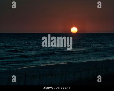 Ein stimmungsvoller Sonnenuntergang über dem Meer oder dem Golf von Mexiko mit einer großen orangefarbenen Kugel direkt über dem Horizont. Stockfoto