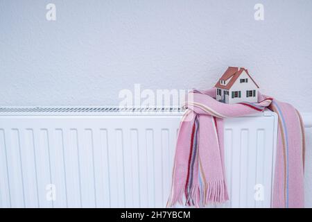 House-Modell in Schal auf Heizkörper im Inneren gewickelt. Heizungssaison Preis Stockfoto