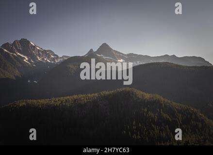 Blick auf schneebedeckte felsige Berggipfel und bewaldete Hügel Stockfoto