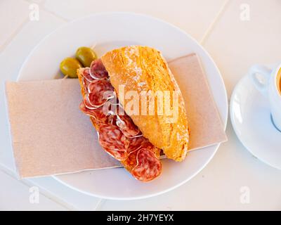 Spanisches Frühstück: Geräuchertes Würstchen-Fuet-Sandwich und Oliven in der Nähe Stockfoto