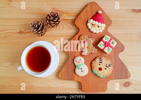 Blick von oben auf verschiedene Weihnachtsplätzchen mit einer Tasse heißen Tee und trockenen Tannenzapfen auf einem Holztisch Stockfoto