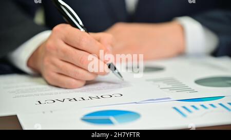 Geschäftsmann prüft Diagramme und Verträge auf dem Schreibtisch Stockfoto