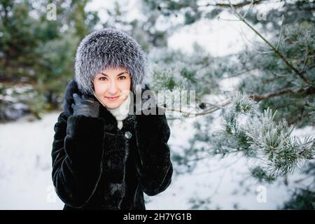 Porträt einer attraktiven lächelnden jungen Frau im Wurmhut im Winter im Freien. Mädchen im Winterwald Stockfoto