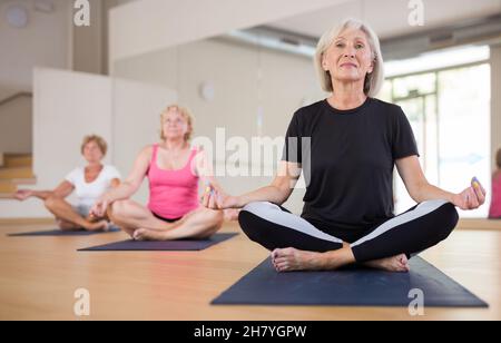 Reife Frau praktiziert Meditation in Lotuspositionen im Yoga-Studio Stockfoto