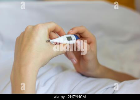 Ein kranker Mensch liegt mit einem Thermometer in den Händen im Bett Stockfoto