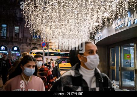 Barcelona, Spanien. 25th. November 2021. Menschen mit Gesichtsmasken gingen unter den Weihnachtslichtern, die auf dem El Corte Inglés-Gebäude in der Nähe der Plaza Catalunya in Barcelona installiert waren.Weihnachtslichter und Dekore, die auf den Plätzen und Straßen in Barcelona installiert waren, erleuchteten die ganze Stadt mit einem Weihnachtsgeist. Dies wird von traditionellen Weihnachtsaktivitäten in Barcelona begleitet. Kredit: SOPA Images Limited/Alamy Live Nachrichten Stockfoto