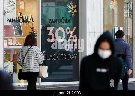 Fußgänger kommen am 26. November 2021 in Tokio, Japan, an einem Schild mit der Aktion „Black Friday“ im Einkaufsviertel von Harajuku vorbei. Einige Geschäfte in Tokio schlossen sich der Black Friday-Schnäppchensaison an, mit Rabatten von 30 % bis 50 % auf ausgewählte Artikel. Quelle: Rodrigo Reyes Marin/AFLO/Alamy Live News Stockfoto