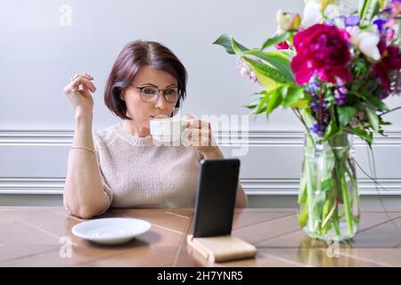 Frau mittleren Alters, die mit einem Smartphone zu Hause sitzt, um sich zu entspannen Stockfoto