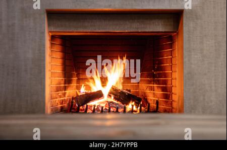 Kamin brennendes Feuerholz. Feuerflammen auf Holzstämmen, Backsteine am Kamin. Gemütliches warmes Zuhause zu Weihnachten, Winterferien Grußkarte Stockfoto