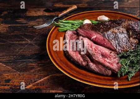 Gerösteter Aufhänger oder Onglet-Rinderfleischsteak in Scheiben auf einem rustikalen Teller mit Hackschnitzel. Dunkler Holzhintergrund. Draufsicht. Speicherplatz kopieren Stockfoto