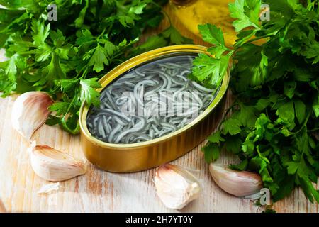 Eingelegte Aale in offener Dose mit Knoblauch am Tisch Stockfoto