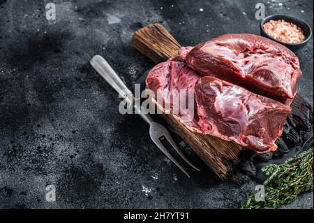 Rohes geschnittes Rind- oder Kalbsherz auf einem Schlachtbrett. Schwarzer Hintergrund. Draufsicht. Speicherplatz kopieren Stockfoto