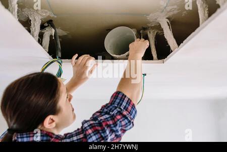 Frau, die Rohr für die Installation der Küchenhaube platziert Stockfoto