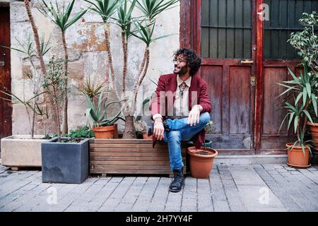 Junger Mann saß vor einem Haus mit vielen Pflanzen um ihn herum Stockfoto