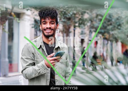 Ein junger Hippanic-Mann, der sein Mobiltelefon an einem bewölkten Tag im Freien benutzt Stockfoto