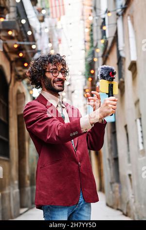 Junger Mann, der mit seinem Mobiltelefon und einem Mikrofon im Freien streamt Stockfoto