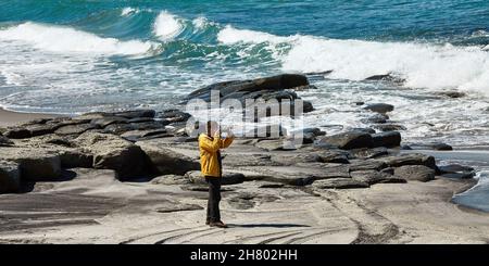 Ein männlicher Fotograf fotografiert vor dem Hintergrund einer wunderschönen Bucht. Die Hintergrundbeleuchtung und der große Raum an Himmel und Bucht schaffen eine ungewöhnliche Atmosphäre Stockfoto