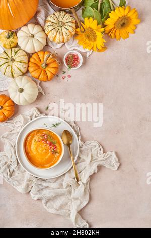 Von oben Schüssel mit leckeren Kürbissuppe mit Granatapfelkernen verziert auf den Tisch mit Gemüse und gelben Sonnenblumen in der Küche gelegt Stockfoto