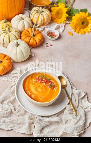 Von oben Schüssel mit leckeren Kürbissuppe mit Granatapfelkernen verziert auf den Tisch mit Gemüse und gelben Sonnenblumen in der Küche gelegt Stockfoto