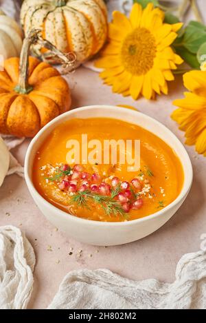 Schüssel mit leckeren Kürbissuppe mit Granatapfelkernen verziert auf den Tisch mit Gemüse und gelben Sonnenblumen in der Küche gelegt Stockfoto