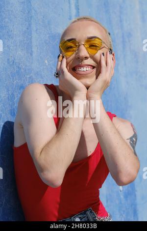 Lächelndes junges nicht-binäres Modell, das an einem sonnigen Tag eine herzförmige Sonnenbrille im Freien trägt. Stockfoto