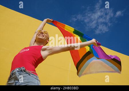 Low-Angle-Ansicht einer jungen nicht-binären Person, die im Freien eine Regenbogenfahne hält und aufhebt. Stockfoto