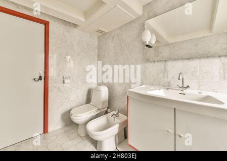 Grau-rotes Badezimmer mit Waschbecken und Spiegel neben der Toilette in hellem, modernem Bad mit gefliester Wand Stockfoto