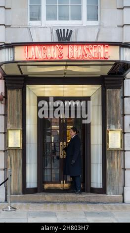 Die Dame an der Tür steht vor dem Haupteingang von Langan's Brasserie. Stratton Street, Mayfair, London, England, Großbritannien Stockfoto