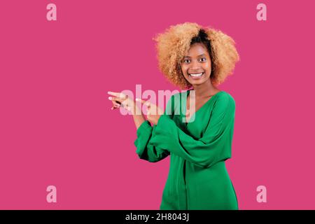 Afro-Frau lächelt und zeigt zur Seite, während sie vor einem bunten Hintergrund steht. Stockfoto
