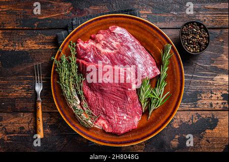 Zwei Lappen oder Flanken rohes Rindfleisch Steaks auf einem rustikalen Teller mit Kräutern. Dunkler Holzhintergrund. Draufsicht Stockfoto