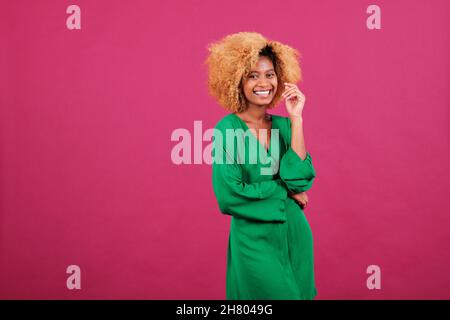 Junge Afro-Frau in stilvollem grünen Kleid lächelt, während sie auf einem isolierten Hintergrund steht. Stockfoto
