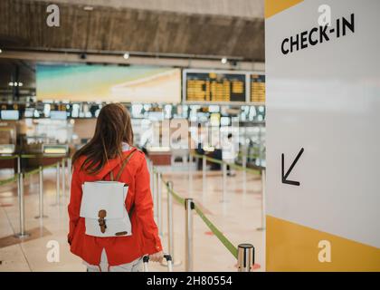 Rückansicht einer nicht erkennbaren weiblichen Reisenden mit Rucksack und Koffer, die vor dem Abflug in der Nähe des Check-in-Schaltes im Flughafenterminal stehen Stockfoto