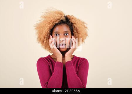 Afro-Frau, die mit einem schockierten Gesichtsausdruck auf die Kamera schaut, während sie auf einem isolierten Hintergrund steht. Stockfoto