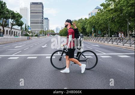 Seitenansicht eines männlichen Hipsters mit Armprothese, der mit dem Fahrrad auf dem Crosswalk in der Stadt läuft Stockfoto