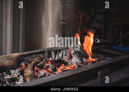 Heiße Flammen aus brennendem Holz in schwarz-metallischem Brazier und glühende Holzkohle, die auf der Terrasse des modernen Cafés aufgestellt wurden, während sie sich zum Kochen vorbereiteten Stockfoto