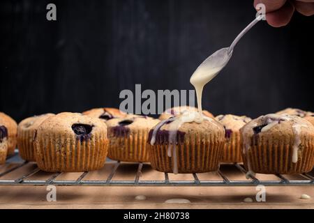 Crop anonyme Person Gießen Sahnehäubchen auf gebackene süße hausgemachte Blaubeer Muffins auf Metall Ofen Rack Stockfoto