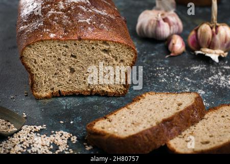 Brot und gesunde Brotscheiben auf dem Tisch mit verstreuten Sesamkörnern und Knoblauchzehen in der Küche Stockfoto
