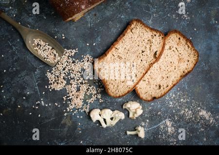 Draufsicht Aufgeschnitten von leckeren frisch gebackenen Blumenkohlebrot auf dem Tisch mit Löffel in verstreuten Sesamkörnern in der hellen Küche Stockfoto