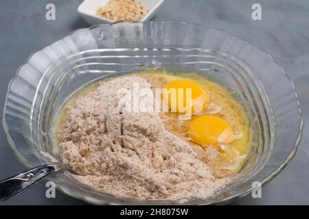 Glasschüssel mit Mehl und zerbrochenen Eiern zum Backen gesunder Bagels, die während des Kochvorgangs in der hellen Küche auf den Tisch gelegt werden Stockfoto