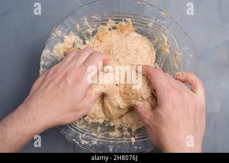 Draufsicht auf die anonyme Person, die Teig für kohlenhydratarme Bagels in einer Glasschüssel auf dem Tisch in der hellen Küche zubereitet Stockfoto