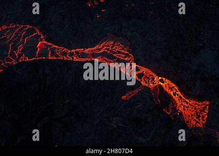 Draufsicht auf heißes rotes Magma, das nachts im Hochland von Island in Dunkelheit auf dunkler Bergoberfläche fließt Stockfoto