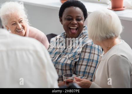 Aufgeregte afroamerikanische Frau, die einen älteren Freund mit Tee im Pflegeheim ansieht Stockfoto