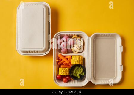 Von oben von Lunch-Boxen mit gesunden Lebensmitteln einschließlich Crackers Karotten Sticks Trauben Kirschtomaten mit Brokkoli-Walnuss und Mandarine auf gelbem Hintergrund Stockfoto