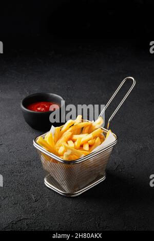 Frische leckere pommes Frites im Korb mit Sauce auf schwarzem Hintergrund Stockfoto