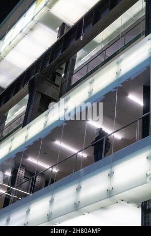 Eine maskierte Frau, die in der Galerie der Tate Modern steht und auf die Haupthalle blickt. London. Stockfoto