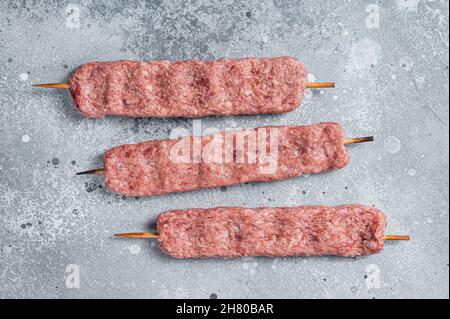 Roher türkischer Adana-Shish-Kebab auf dem Metzgertisch. Grauer Hintergrund, Draufsicht Stockfoto