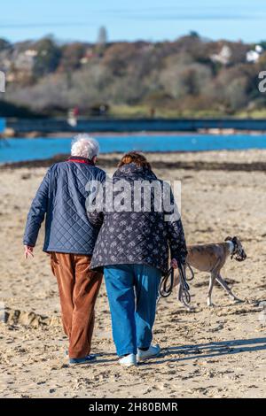 Ein älteres Paar, das auf einer Insel von wight Beach an der Küste von bembridge spaziert, ein Rentnerpaar, das mit seinem Hund am Strand oder Sandstrand entlang läuft. Stockfoto